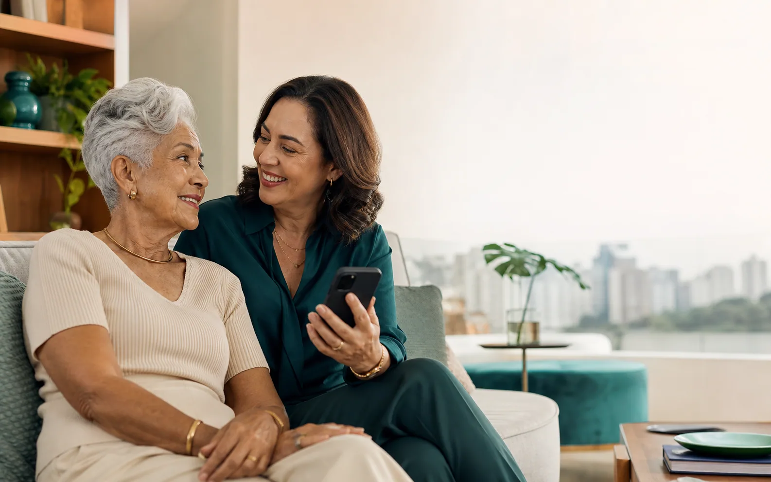 Filha e mãe idosa sentadas juntas no sofá, conversando com um celular na mão